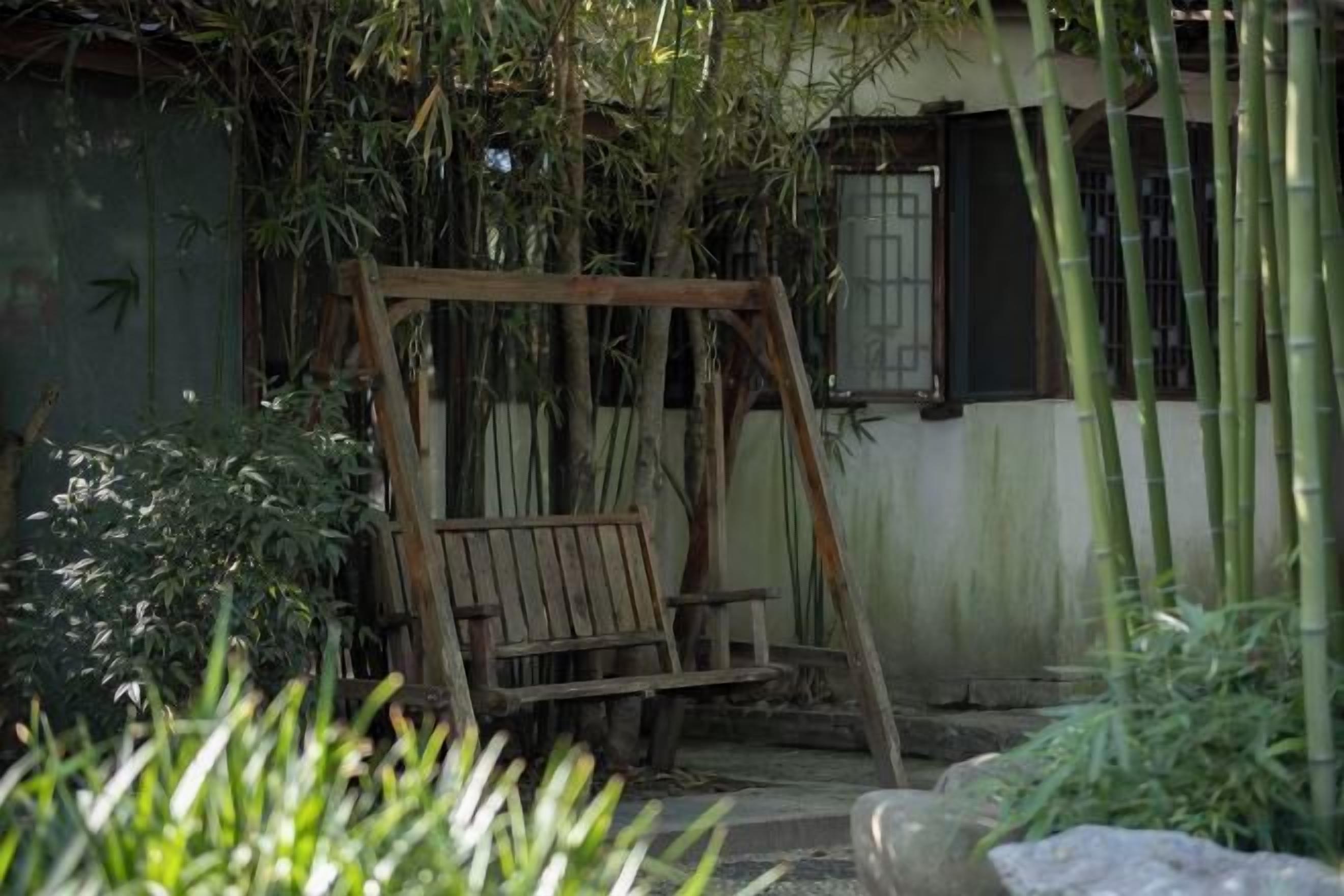 Ein hölzernes Schaukelgestell in einem Garten mit Bambuspflanzen und einem Gebäude im Hintergrund.