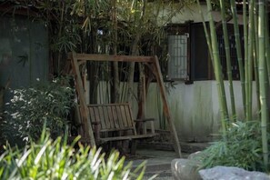 Un conjunto de columpios de madera en un jardín con plantas de bambú y un edificio al fondo.