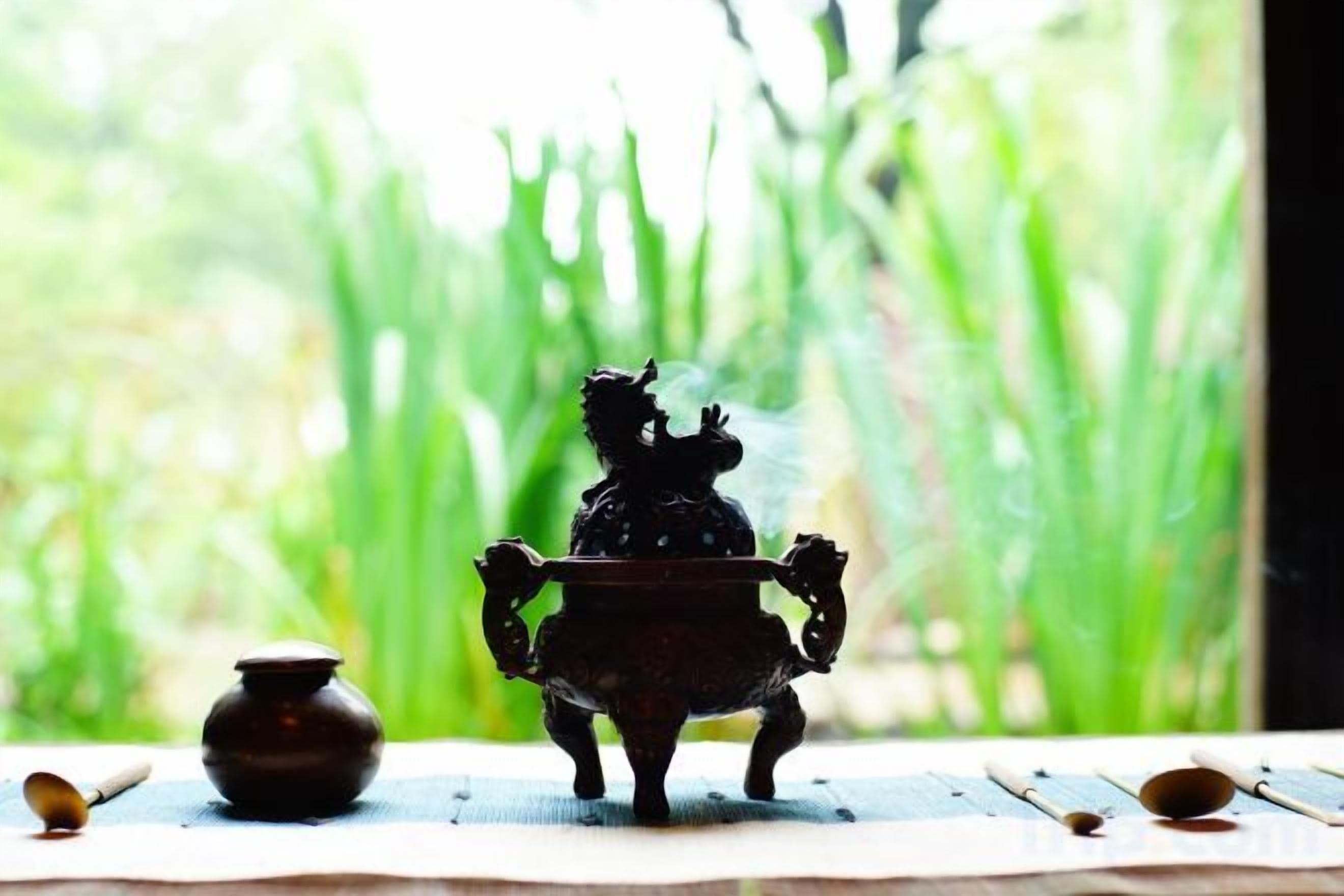 A small, dark-colored, ornate object resembling a horse on a stand, with a pot and spoon nearby on a wooden surface.