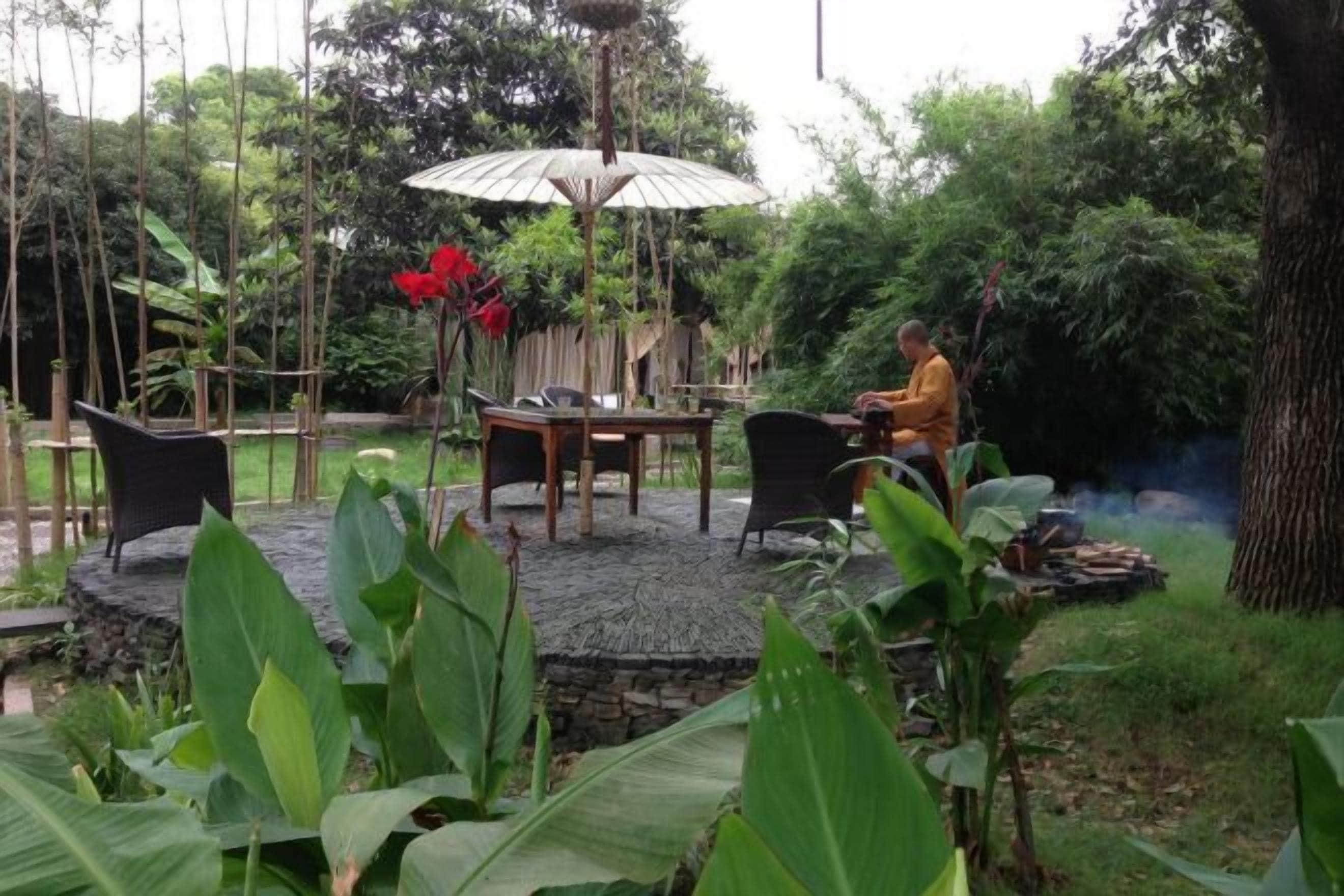 An outdoor seating area with a table and chairs, surrounded by greenery and a bamboo fence.