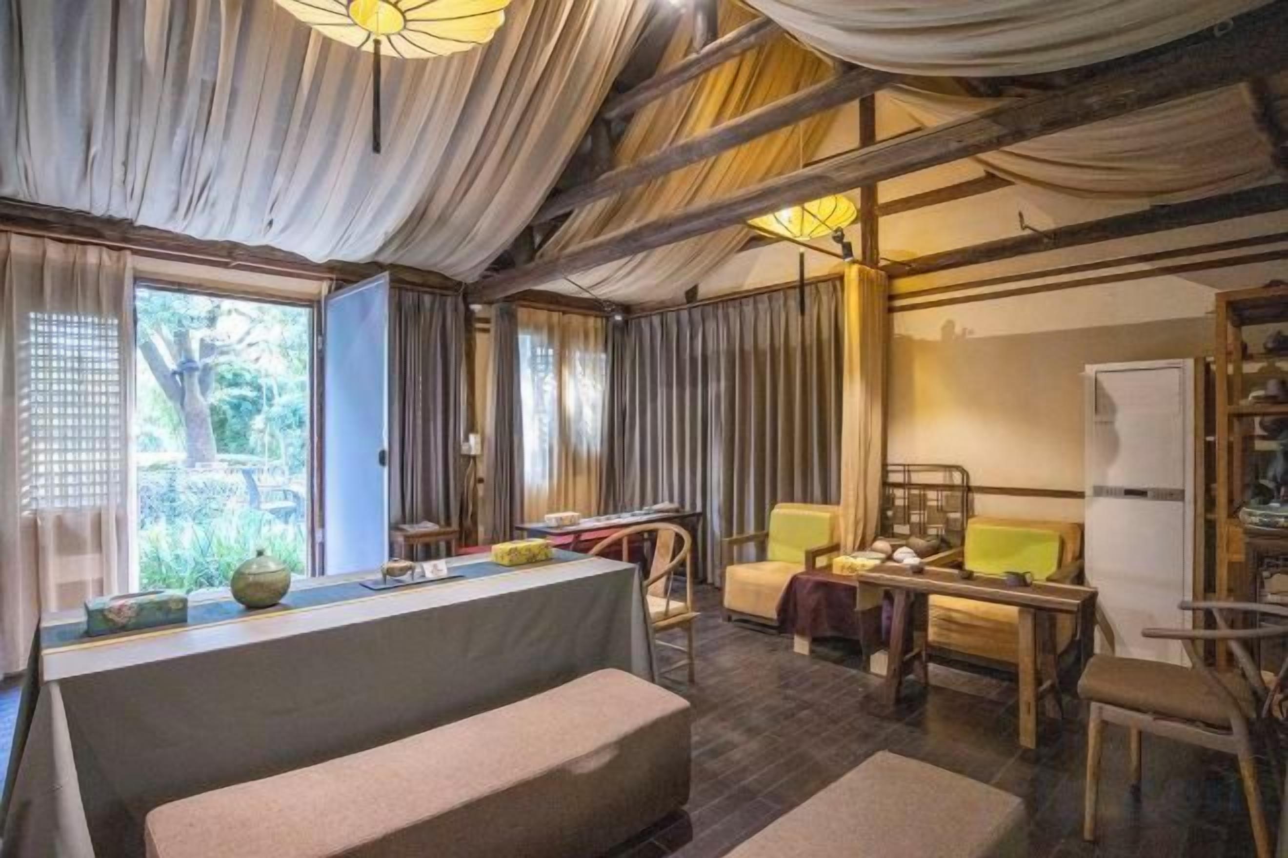 A room with a wooden ceiling, a sofa, a dining table, and a refrigerator.