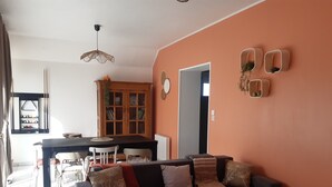 A living room with a dark sofa, a dining table, and a kitchen area in the background. - "Chez Christine," a Picardy Farmhouse, Fully Equipped for a Family Vacation. (Le Meillard)