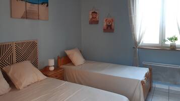 Une chambre avec deux lits, une tête de lit en bois, une table de chevet, une lampe, une fenêtre avec des rideaux et des œuvres d’art murales.