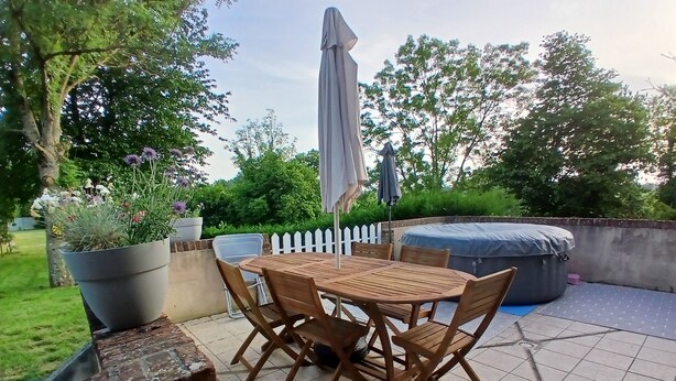A patio with a wooden table and chairs, a potted plant, a white picket fence, and a covered seating area. - "Chez Christine," a Picardy Farmhouse, Fully Equipped for a Family Vacation. (Le Meillard)