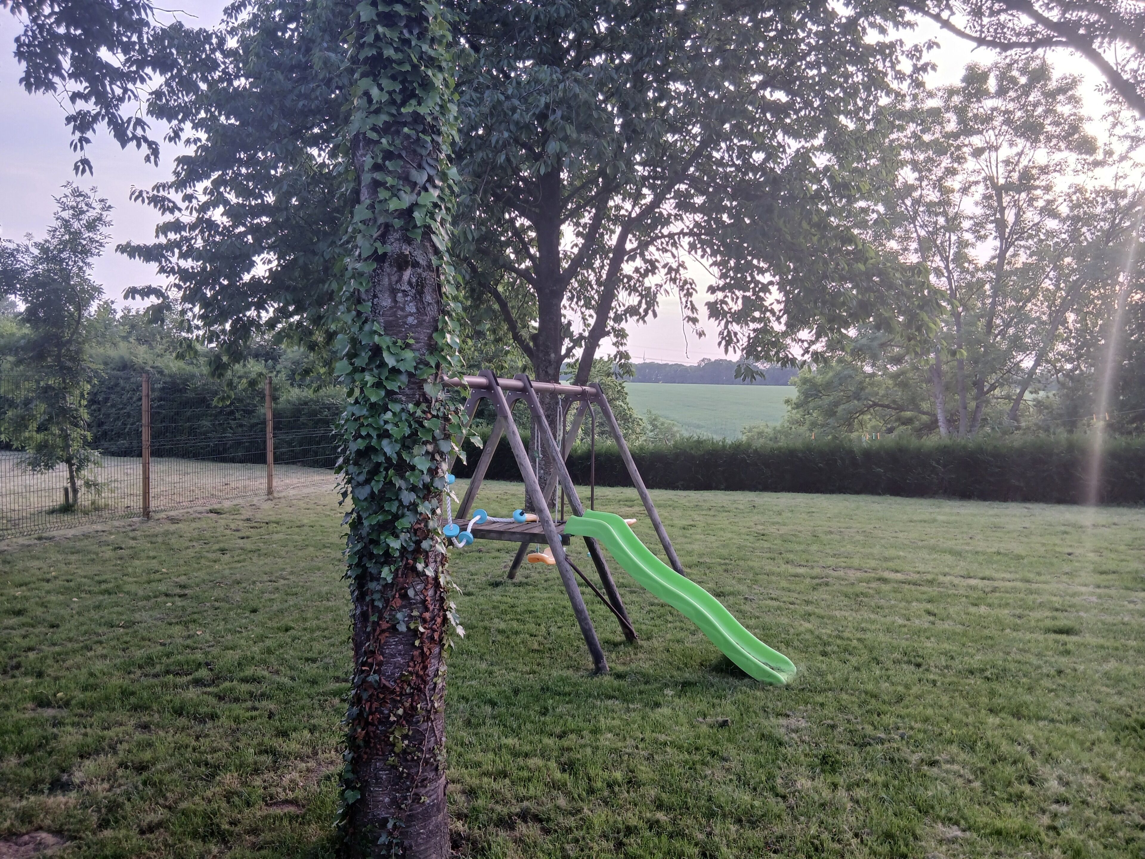 Un parque infantil con columpios y un tobogán, rodeado de césped y árboles.