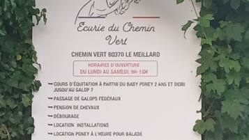Schild für 'Ecurie du Chemin Vert' mit Annehmlichkeiten wie Reiten, Reitzentrum und einer Kontaktnummer.