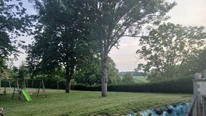 A grassy backyard with a swing set, trees, and a garden bed with plants. - "Chez Christine," a Picardy Farmhouse, Fully Equipped for a Family Vacation. (Le Meillard)