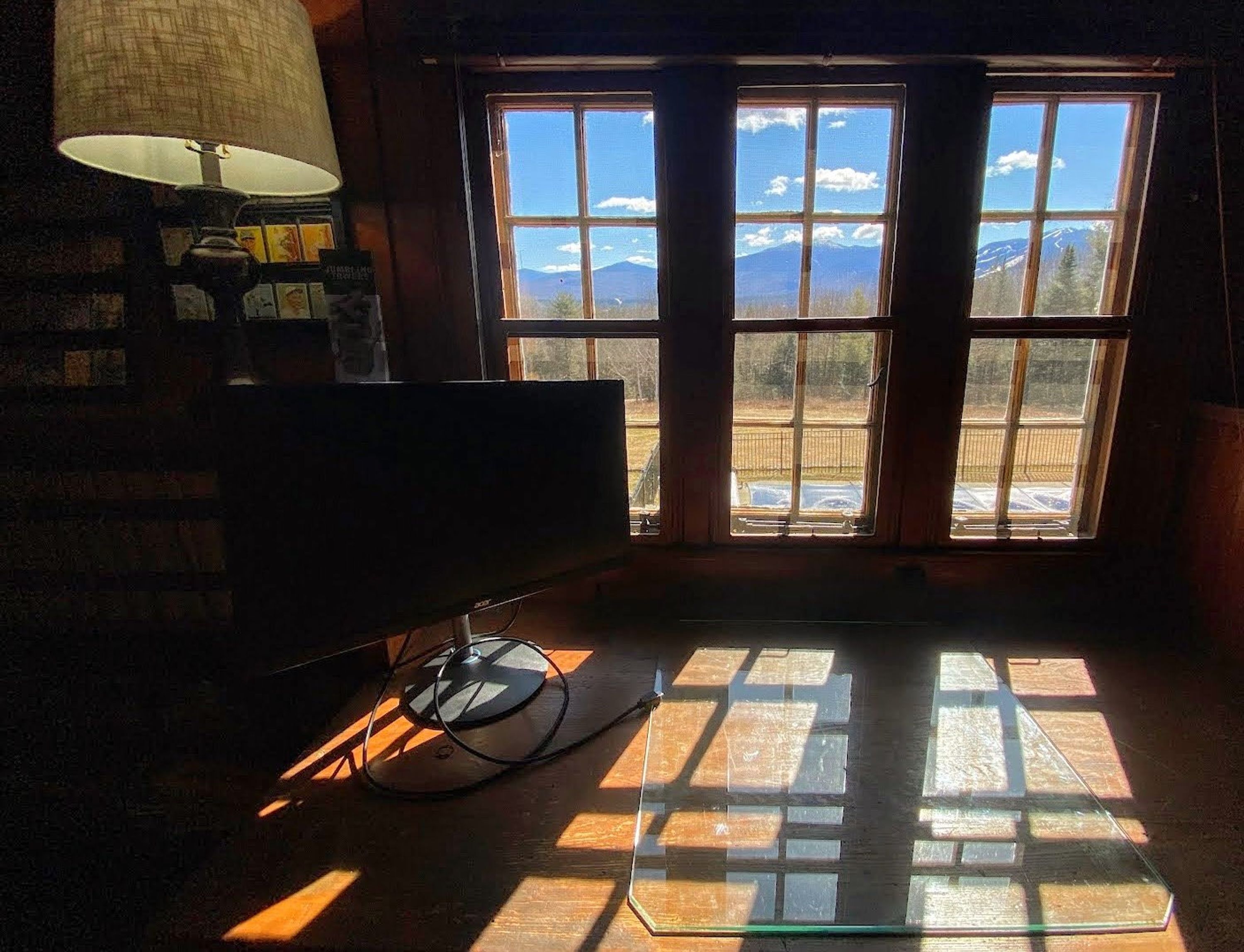 A room with a desk, lamp, and a view of mountains through large windows.