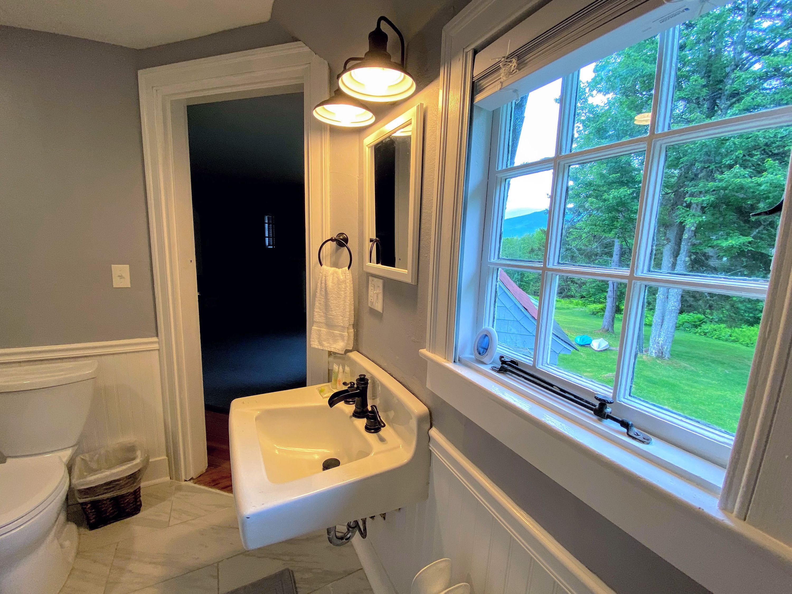 Un bagno con lavandino bianco, uno specchio e una finestra.