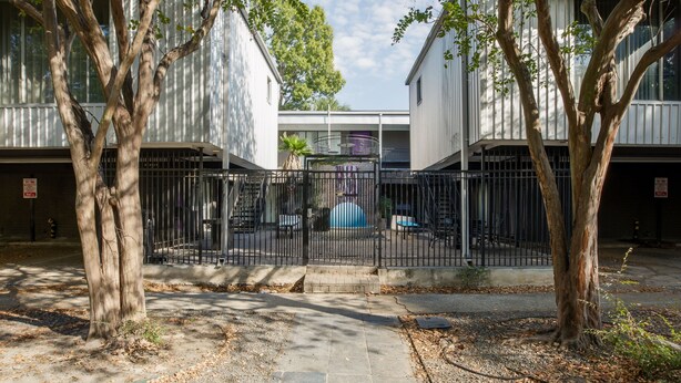 A gated courtyard with a paved walkway, surrounded by trees and buildings with white exteriors. - 1BR W Alabama Montrose Sueño Apt 6, Med Center! (Houston)
