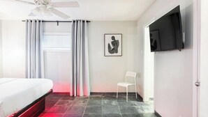 A bedroom with a bed, a chair, a ceiling fan, a TV, and a painting on the wall. - 1BR W Alabama Montrose Sueño Apt 6, Med Center! (Houston)
