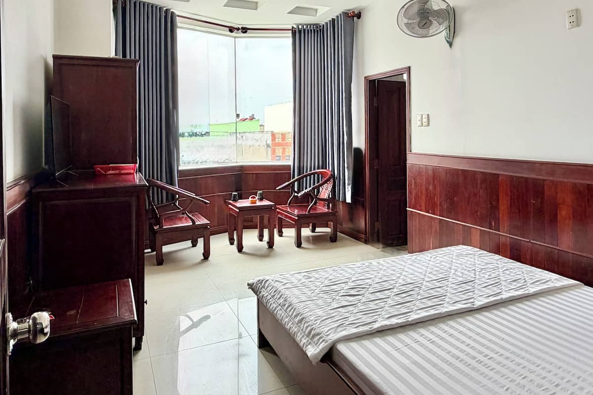 Una camera d'albergo con un letto, una scrivania, due sedie, una TV e una finestra con tende.
