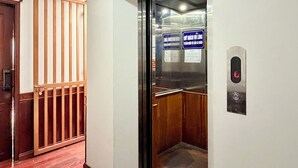 Een lift met een digitaal scherm, een houten deur en een metalen leuning.
