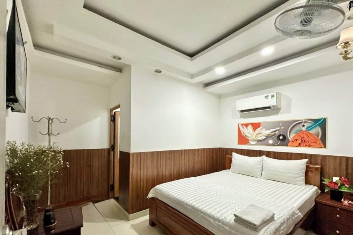 Una camera da letto con un letto in legno, biancheria bianca, un condizionatore d'aria e un quadro appeso al muro.