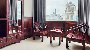 Een kamer met een groot raam, houten meubels en uitzicht op gebouwen.
