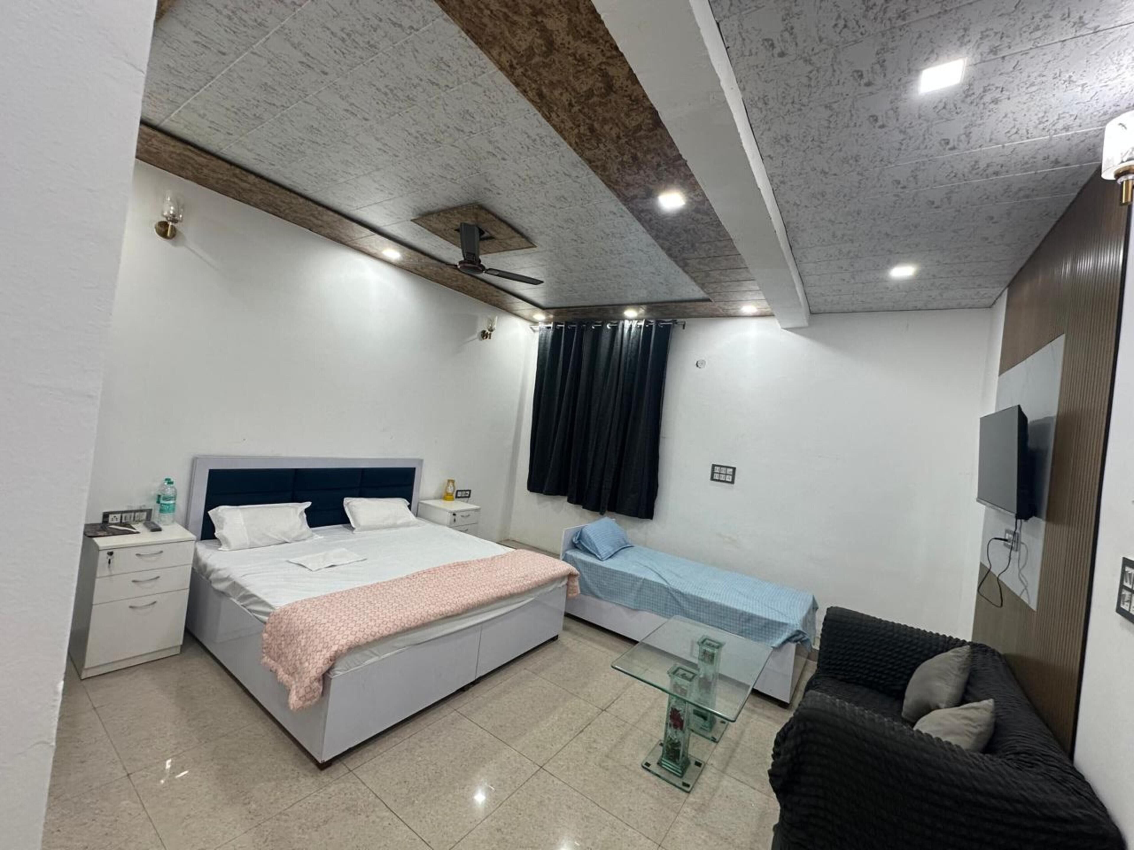 A bedroom with a bed, bedside tables, a glass coffee table, a sofa, a TV, and a ceiling fan.