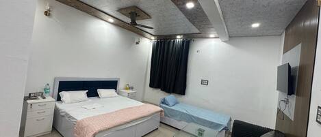 A bedroom with a bed, bedside tables, a glass coffee table, a sofa, a TV, and a ceiling fan.