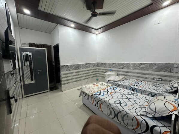 A room with two beds, a wardrobe, a ceiling fan, and a tiled floor. - The Luxe Haven (Sonepat)