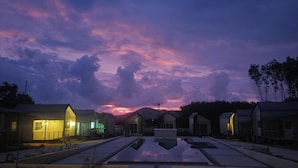 A series of modern, single-story buildings with a reflective pool in the center, surrounded by trees and a sunset sky. - Nararin.Phuket/ Family house (Phuket)