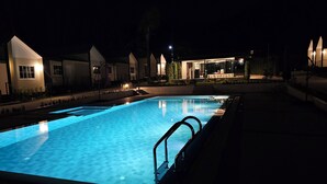 A swimming pool with a blue-lit deck, adjacent buildings with a modern design, and a clear night sky. - Nararin.Phuket/ Family house (Phuket)