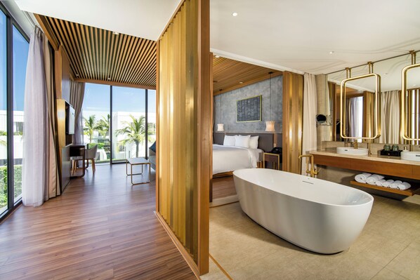 A modern hotel room with a large bathtub, a dining area with a view, and a well-equipped bathroom.