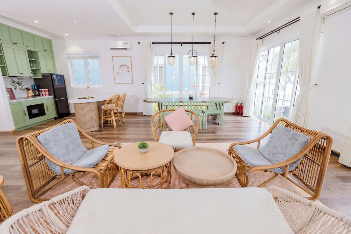 A modern kitchen with green cabinets, a dining area with wicker furniture, and a large window providing natural light.