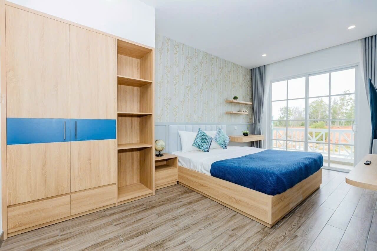 Un dormitorio con cama, armario, mesita de noche y ventana con cortinas.