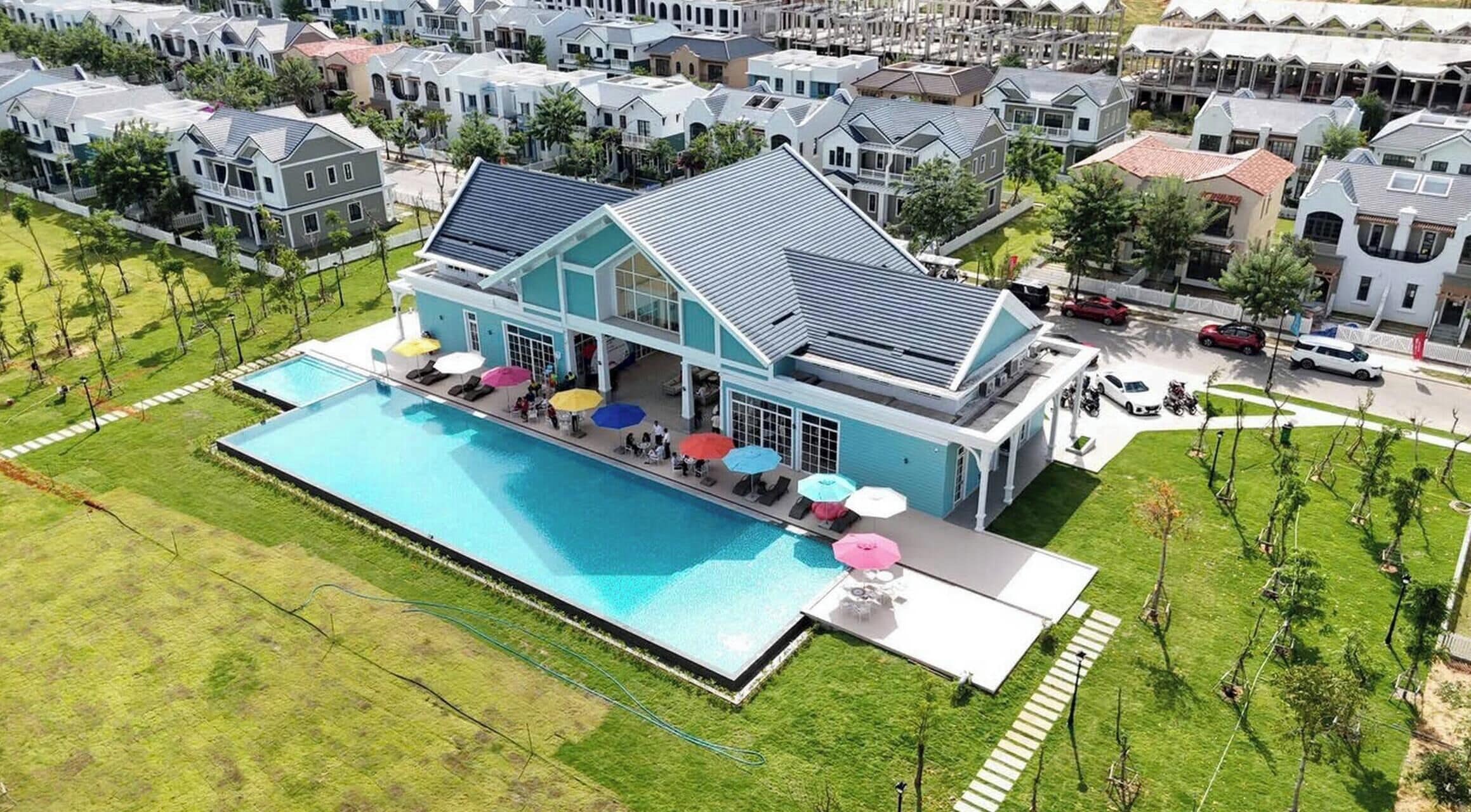 Una casa grande con piscina, múltiples sombrillas y un césped bien cuidado.
