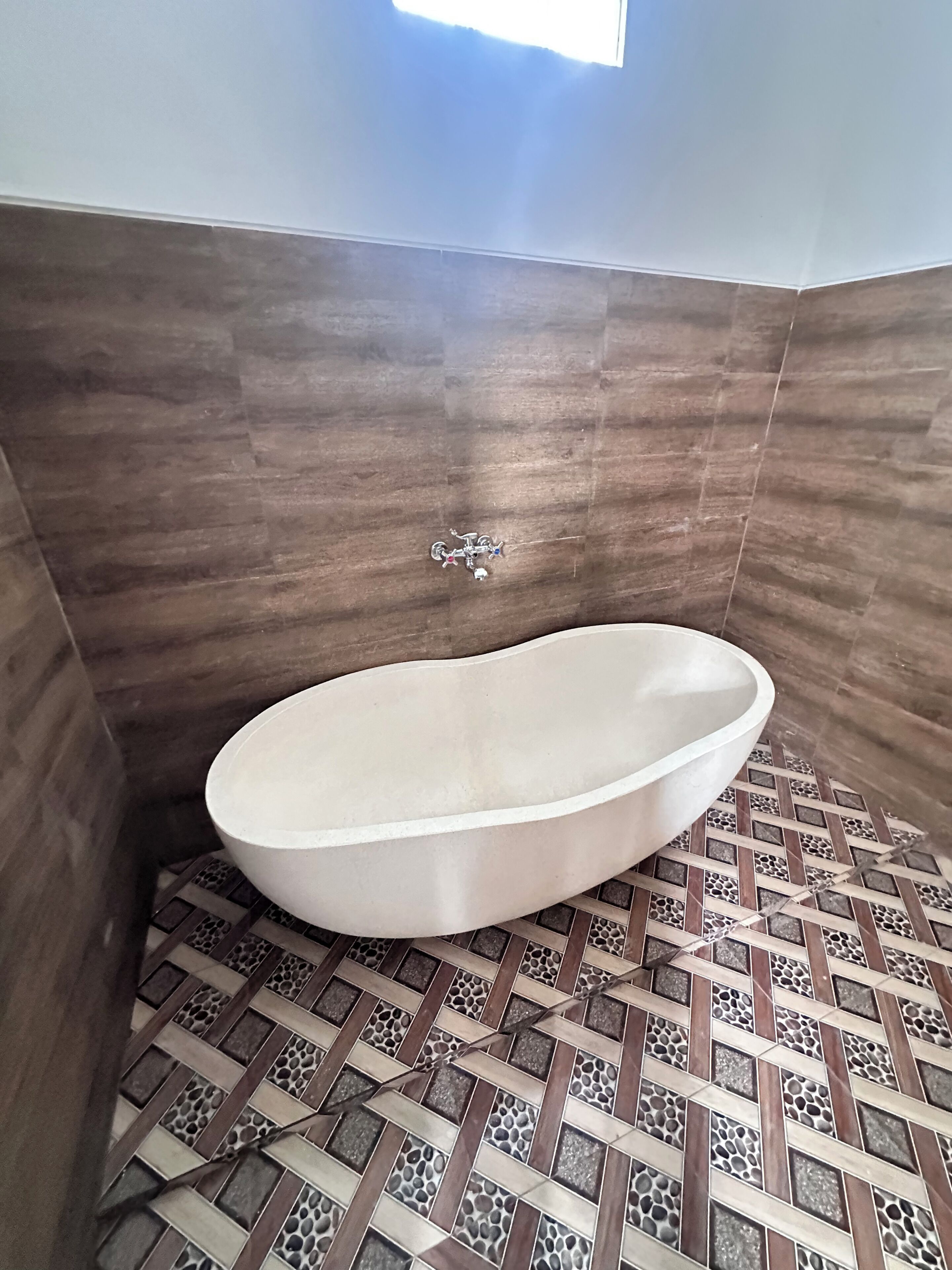 Een badkamer met een vrijstaand bad, betegelde vloer en een raam.
