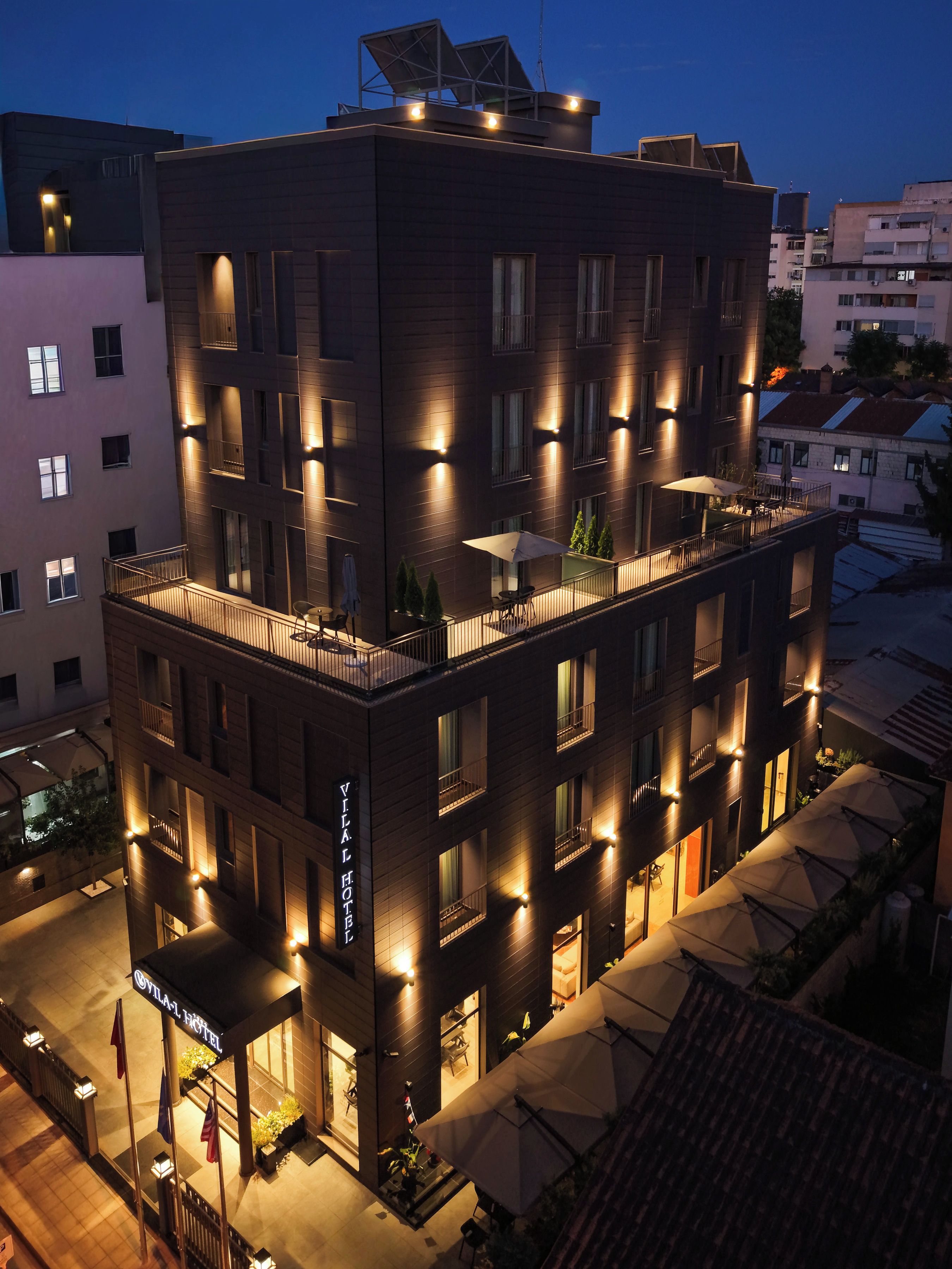A multi-story hotel with a modern design, featuring balconies, outdoor seating, and a well-lit facade.