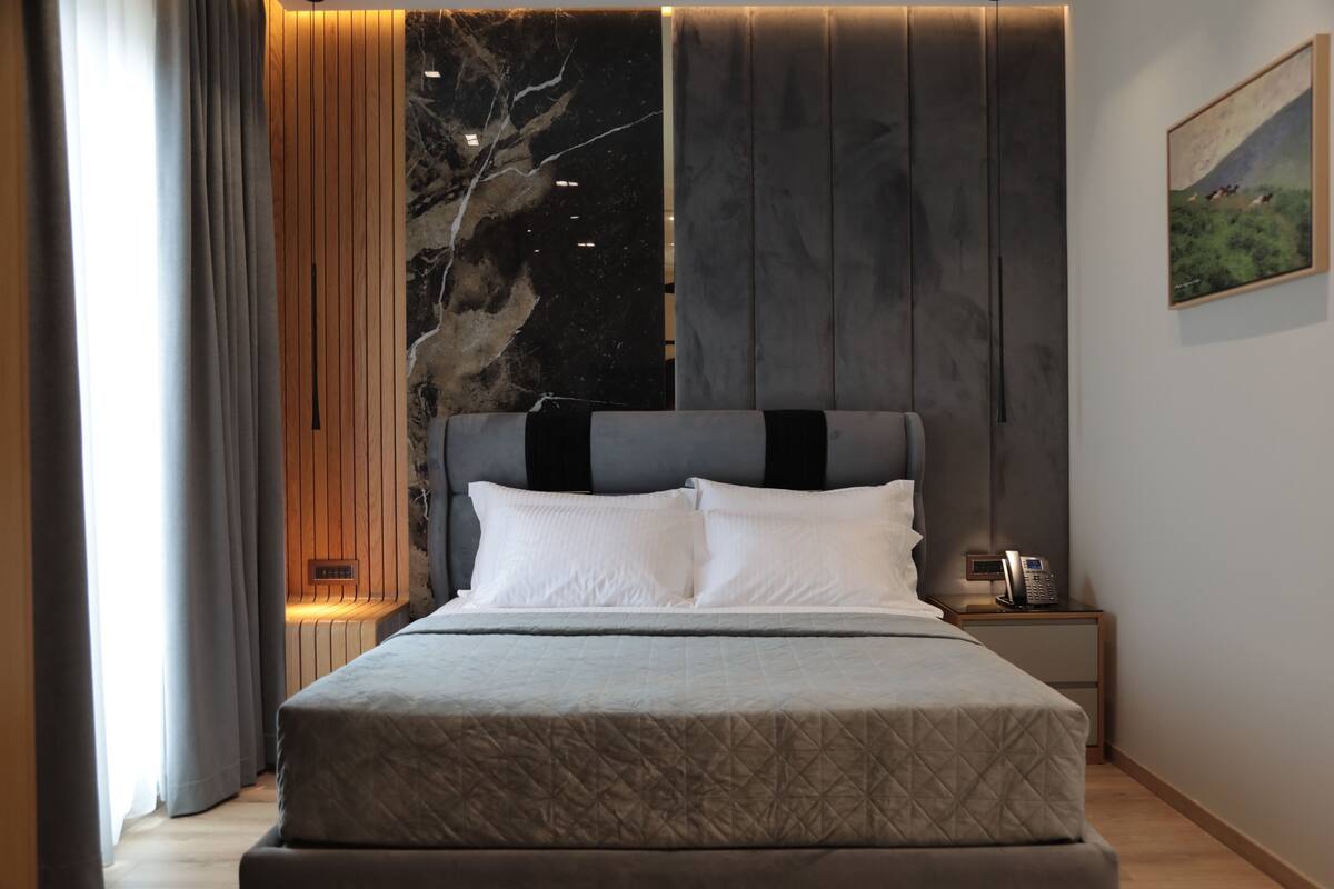 A modern bedroom with a large bed, a nightstand, a telephone, and a painting on the wall.