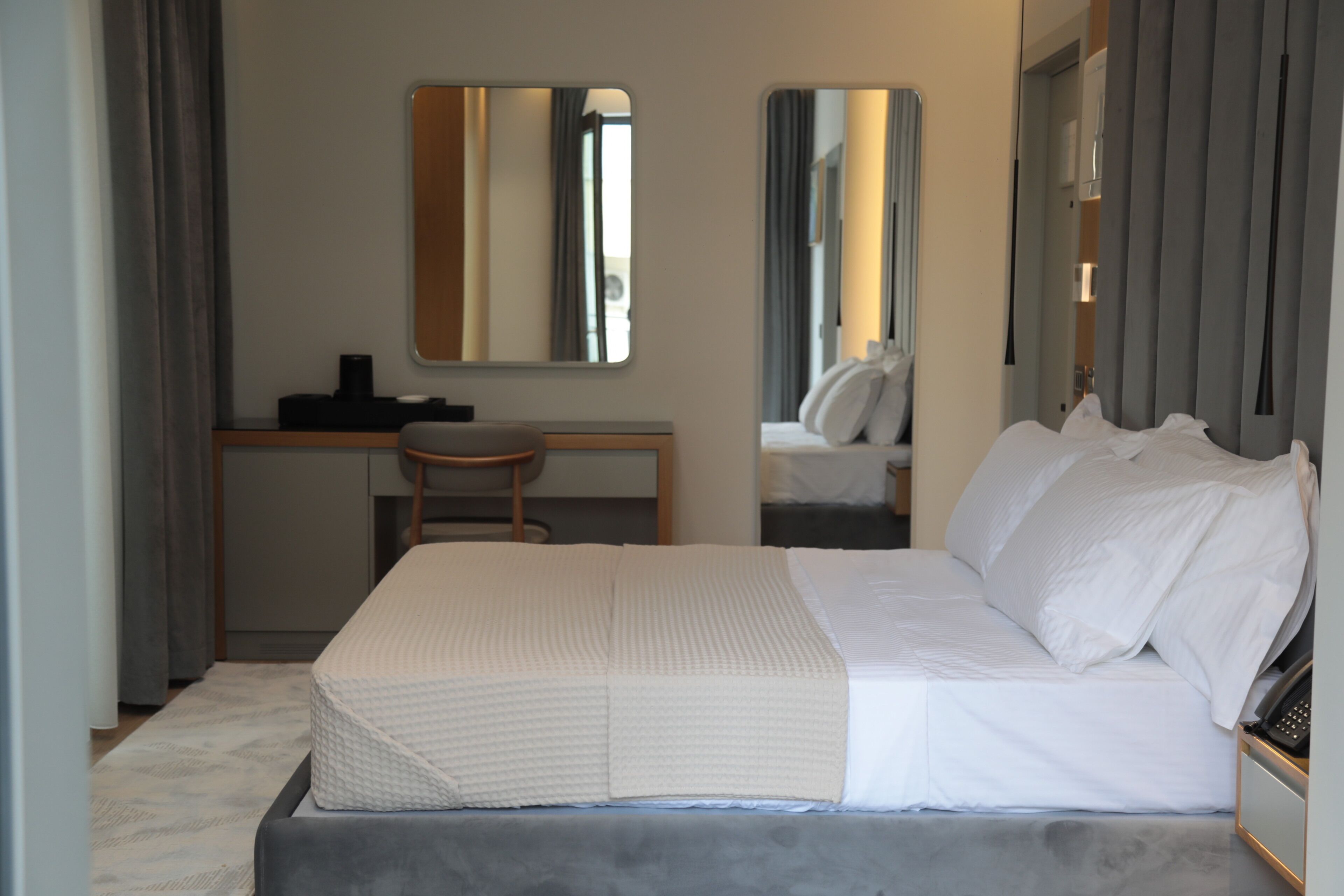 A hotel room with a bed, a desk, a chair, and a mirror.
