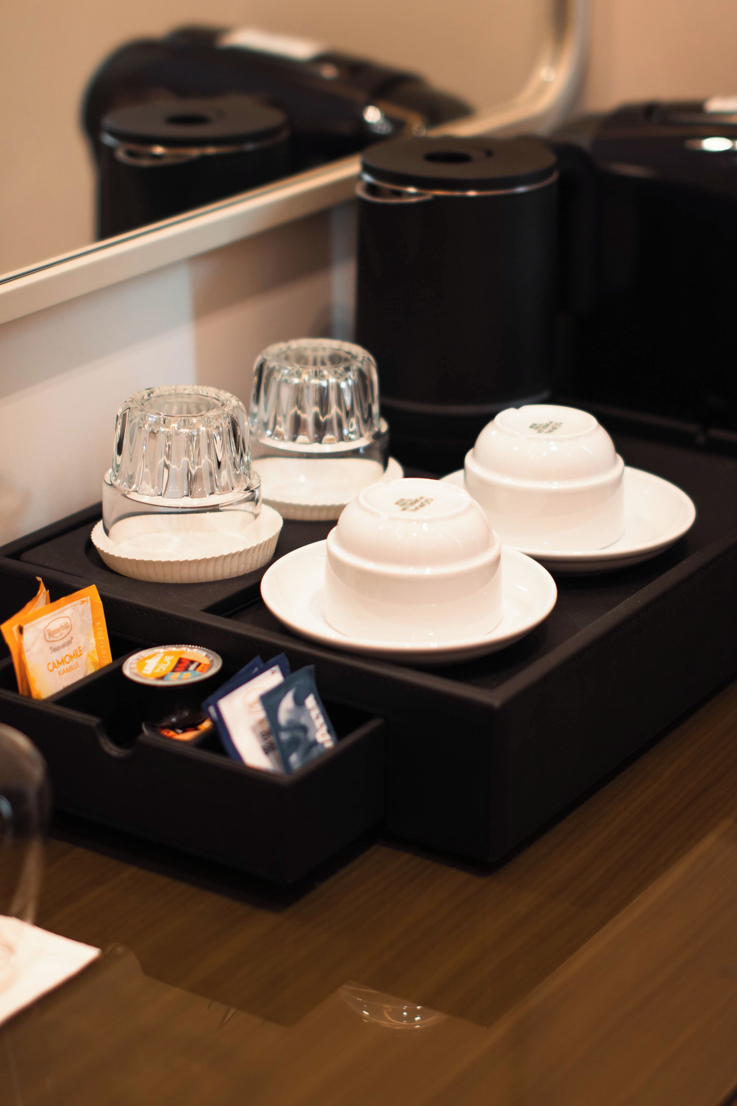 A tray with teacups and a teapot, a glass carafe, and a small tray with tea bags and a packet.