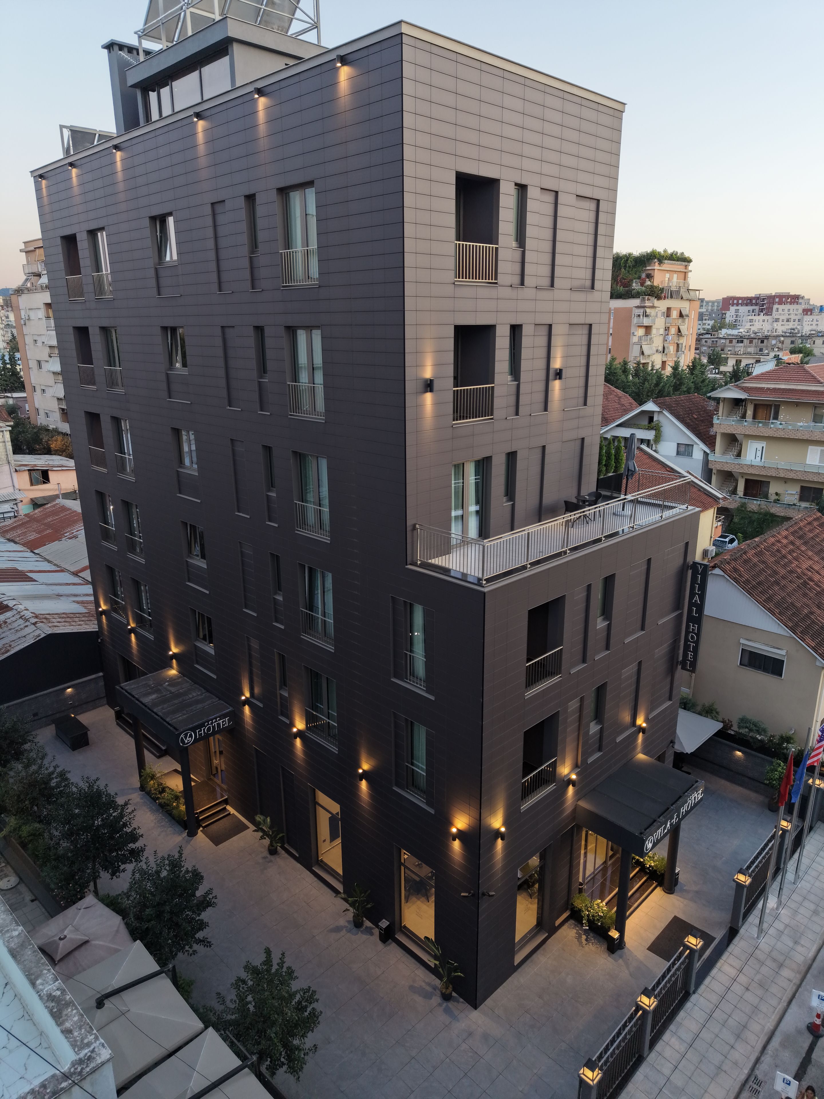 Un hôtel à plusieurs étages, doté d’un design moderne, comprenant des balcons, un espace extérieur couvert avec des sièges et une enseigne indiquant le nom « Yilal Hotel ».