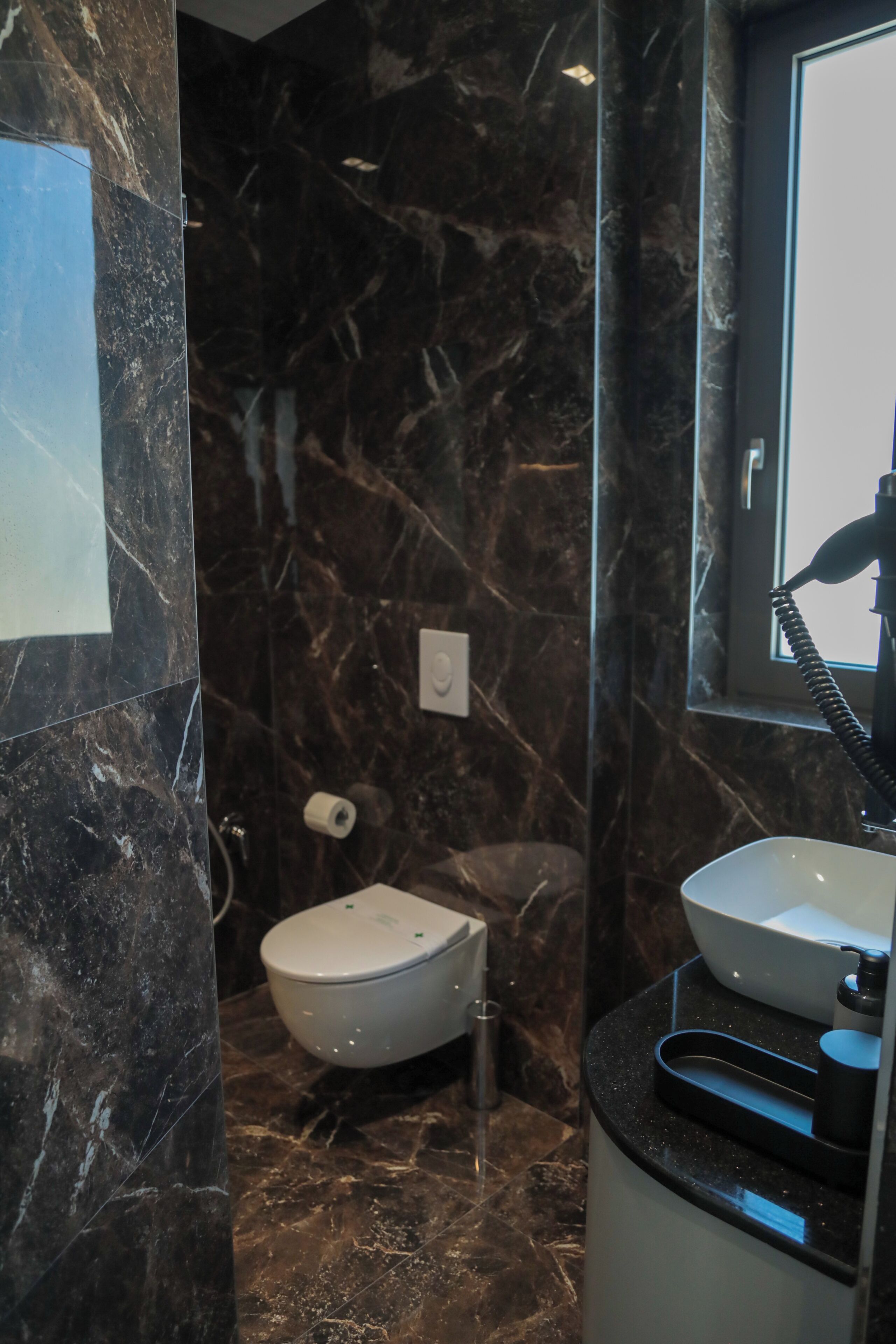 Een badkamer met toilet, wastafel en marmeren wanden.