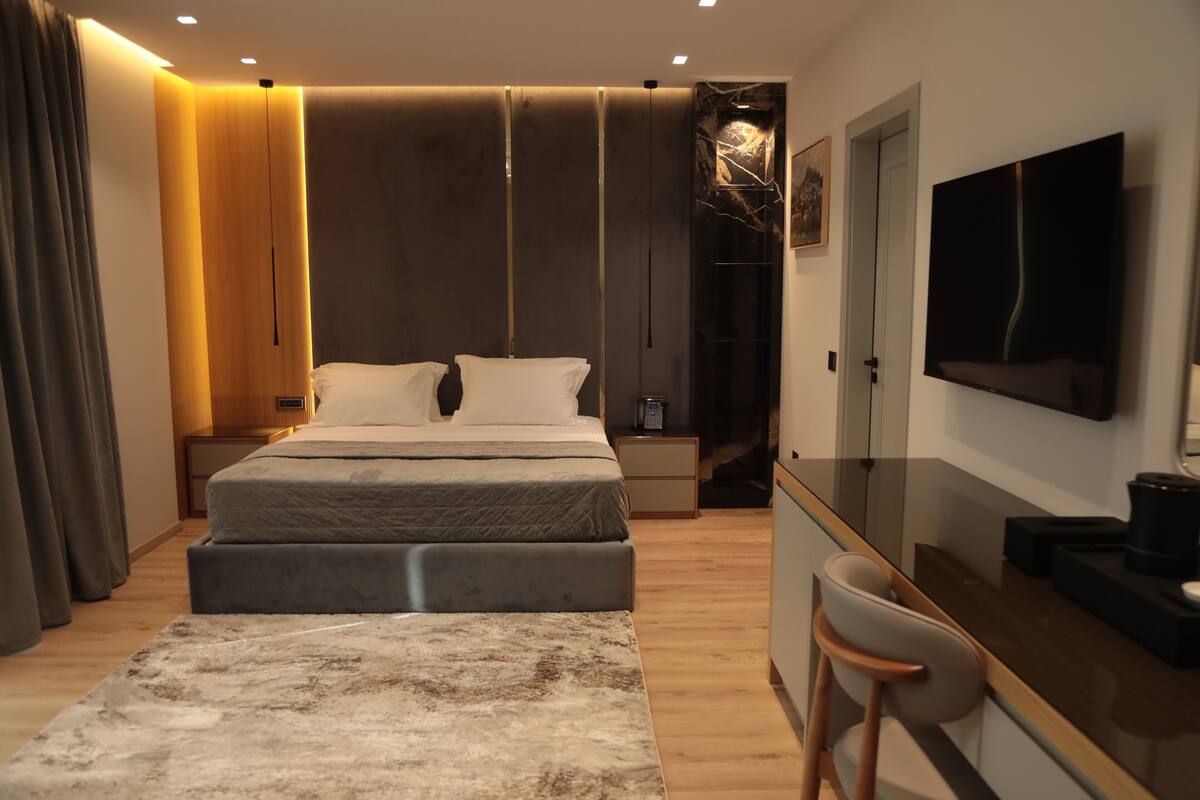 A modern bedroom with a large bed, bedside tables, a TV, and a desk area.