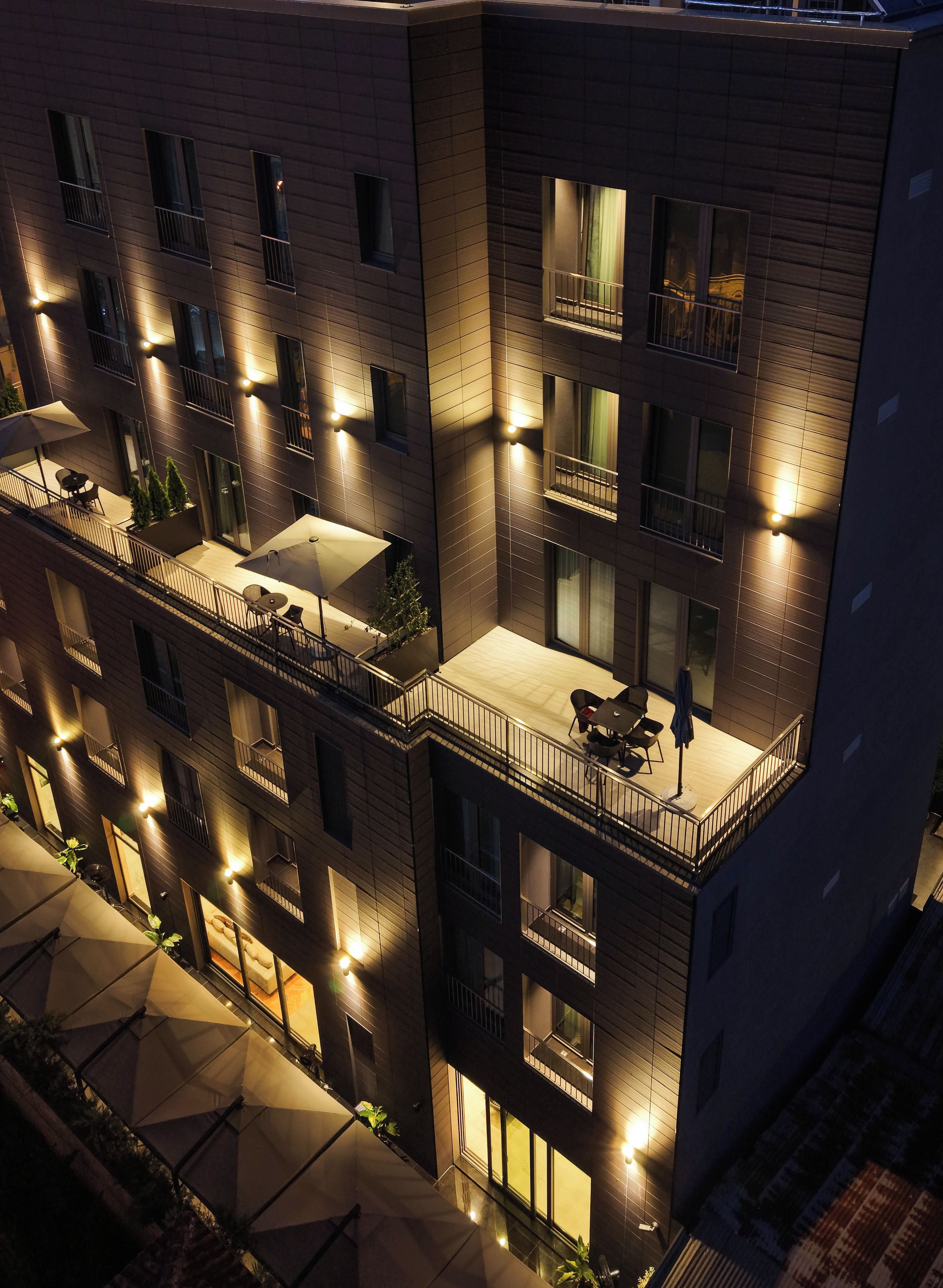 Un immeuble à plusieurs étages doté de balcons, d’un espace extérieur aménagé pour s’asseoir et de fenêtres illuminées.