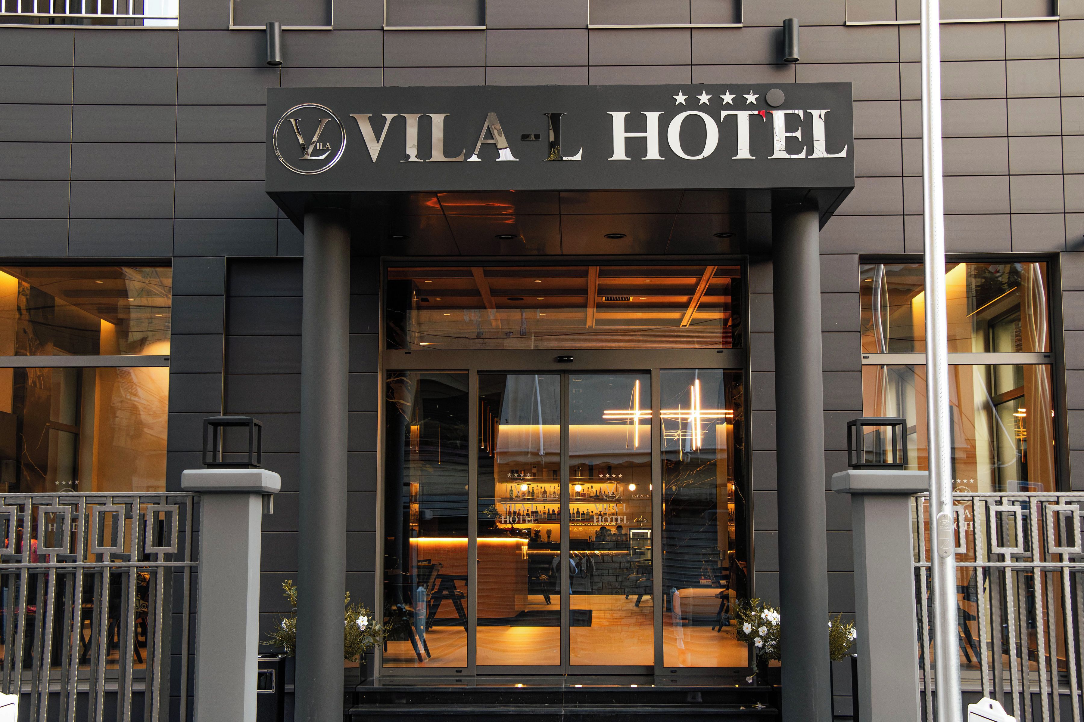 Entrada de hotel com design moderno, exibindo uma placa chamativa sobre a porta e uma área de recepção visível no interior.