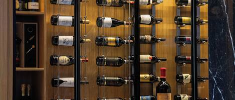 Una botellera con varias botellas, un estante de madera y una superficie de mármol.