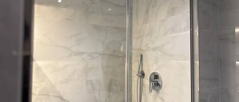 A glass-enclosed shower with a marble wall, a handheld showerhead, and a wall-mounted faucet.