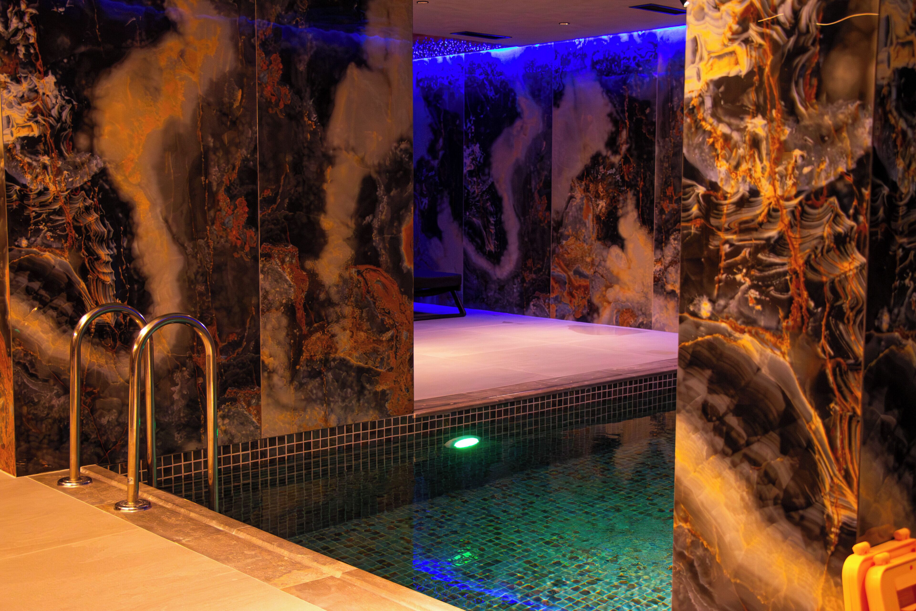A spa area with a hot tub, tiled walls, and a blue ambient light.