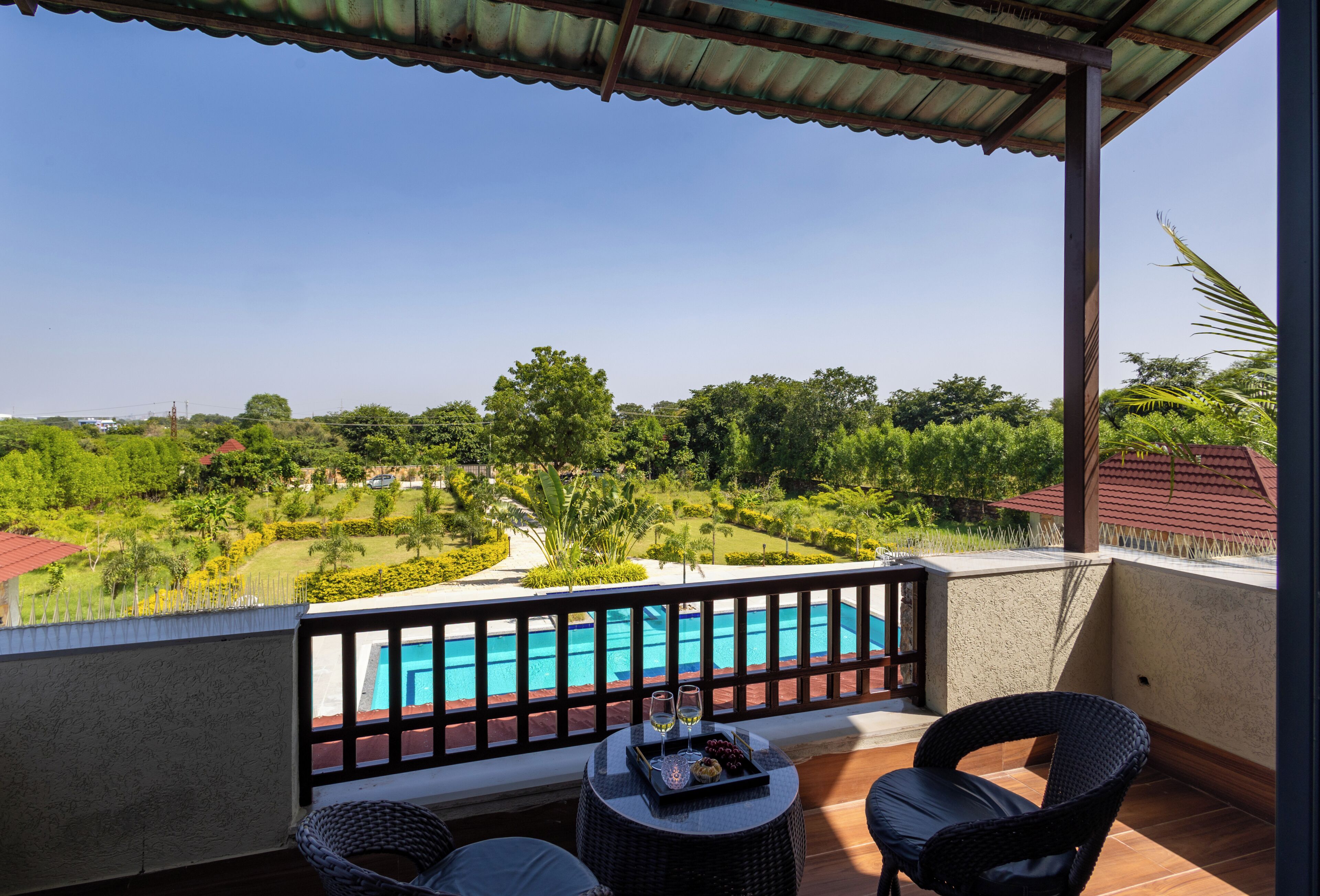 Un balcon donnant sur une piscine, deux fauteuils en osier et une petite table sur laquelle se trouvent une assiette de raisins et un verre de vin.