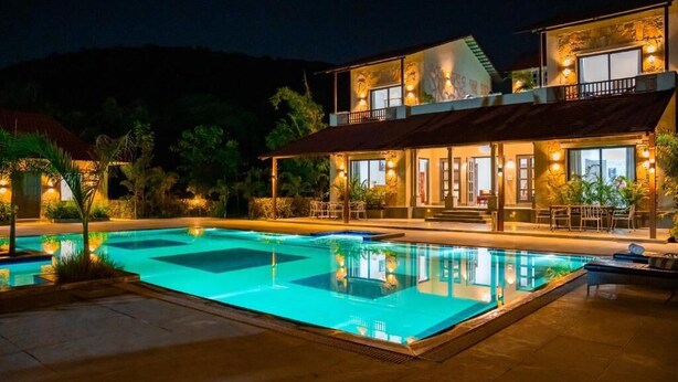 Un hotel con piscina, mobiliario exterior y montañas al fondo.