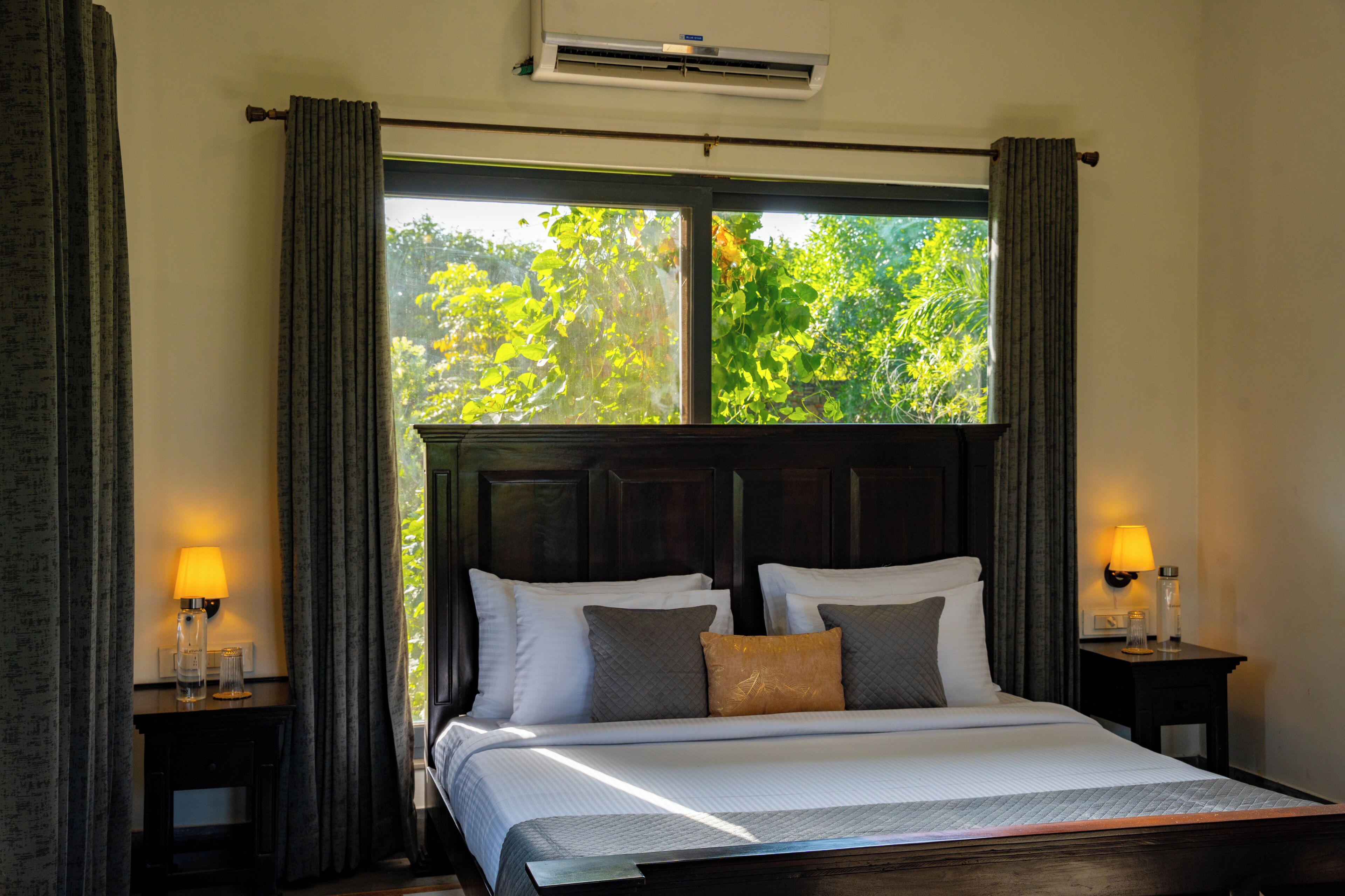 Une chambre d’hôtel avec un grand lit, deux tables de chevet avec des lampes, une fenêtre avec des rideaux et un appareil de climatisation.