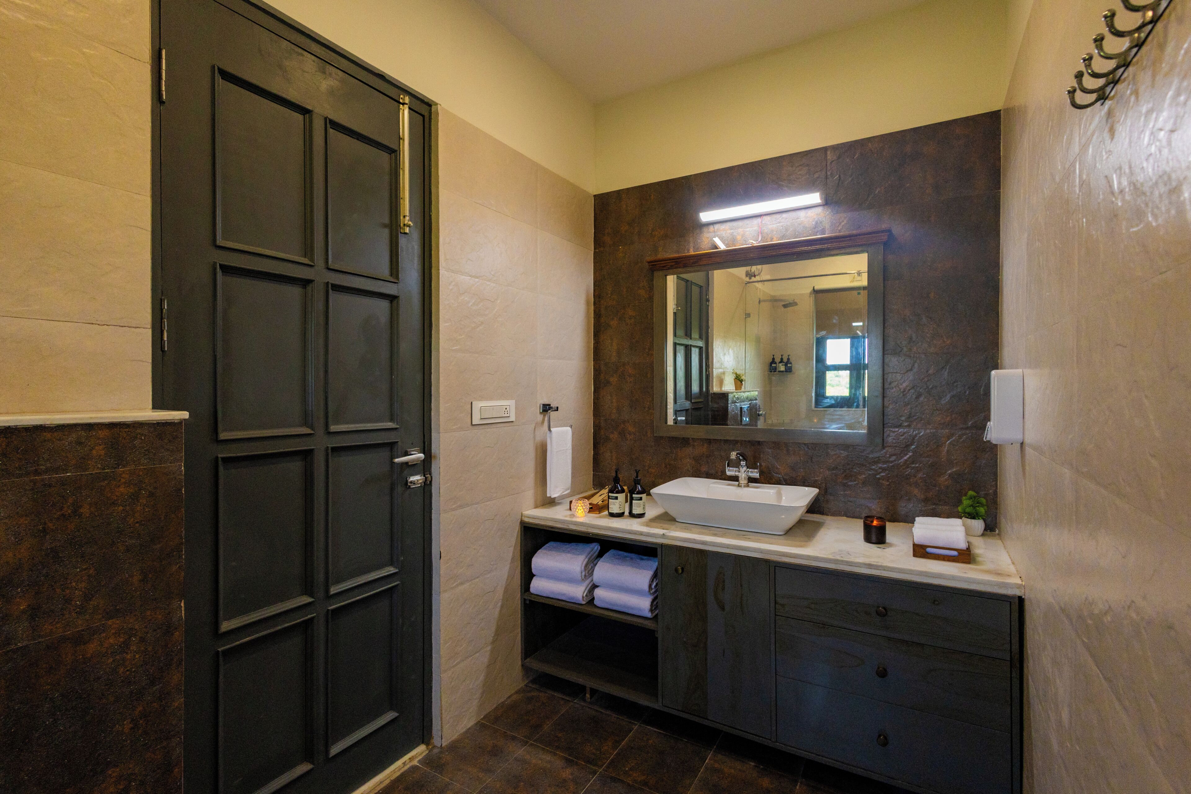 A bathroom with a dark door, a large mirror, a white sink, and a towel rack.