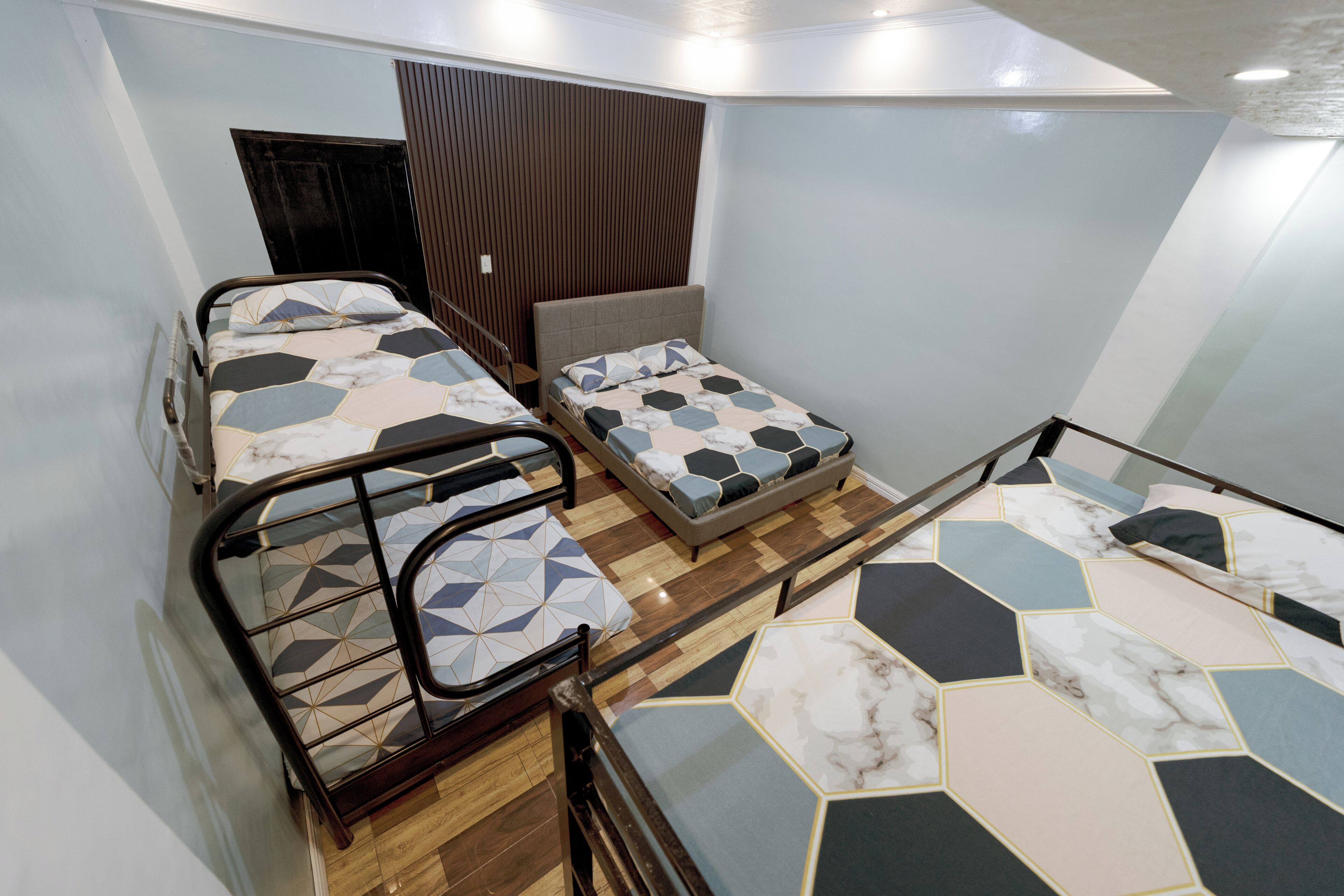 A room with three beds, wooden flooring, and a sloped ceiling.