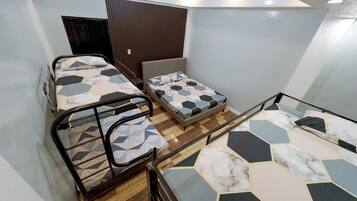A room with three beds, wooden flooring, and a sloped ceiling.