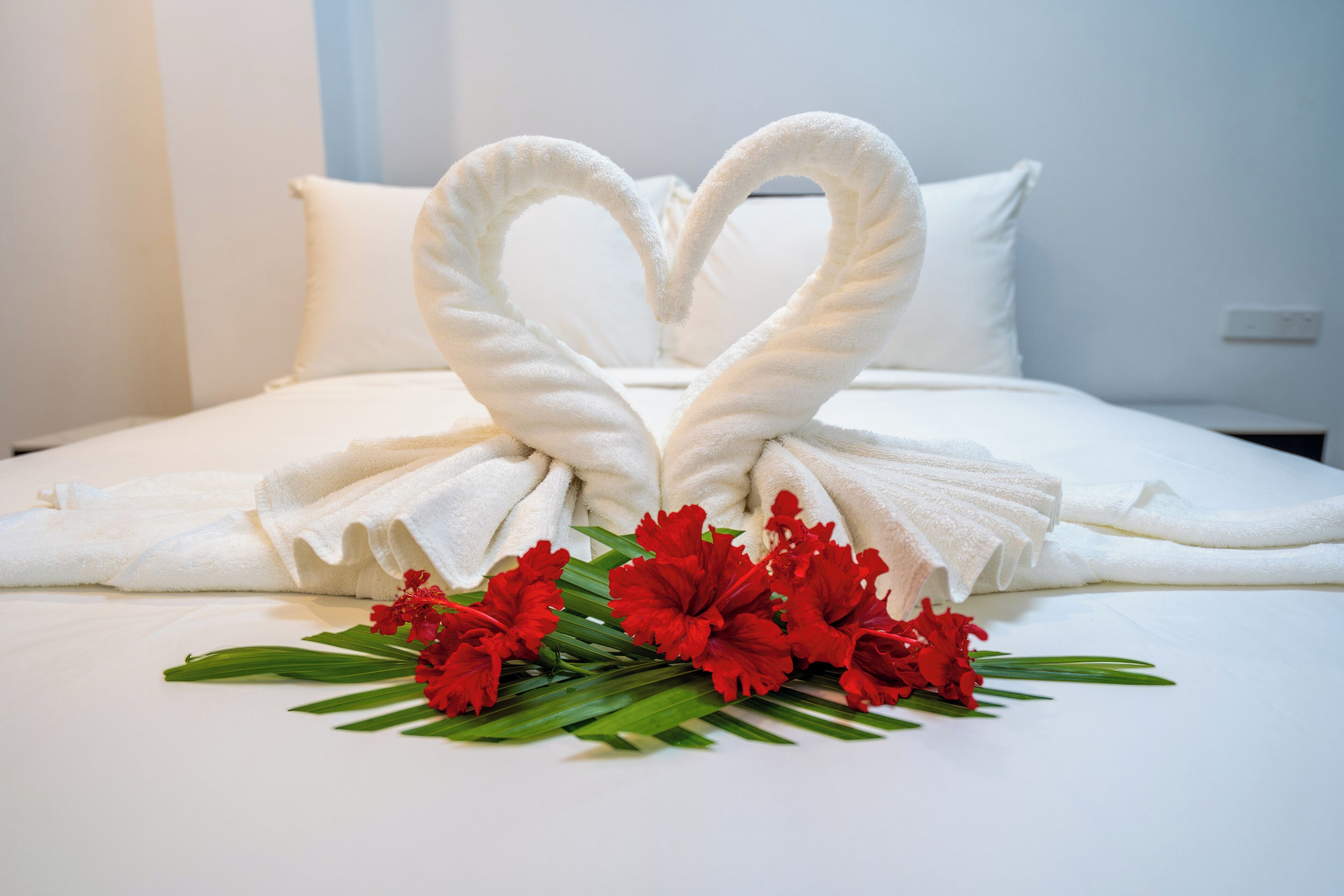 Ein Bett mit weißen Leinen, eine herzförmige Handtuchgestaltung und rote Blumen.