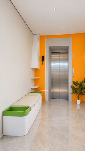 Um elevador moderno com acabamento metálico, uma parede branca com estante e um banco verde.