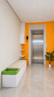 Un ascensor moderno con detalles metálicos, una pared blanca con estanterías y un banco verde.